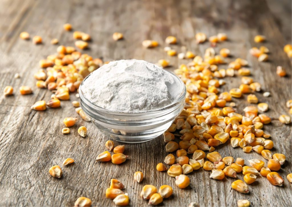 Glass bowl filled with maltodextrin surrounded by scattered corn kernels