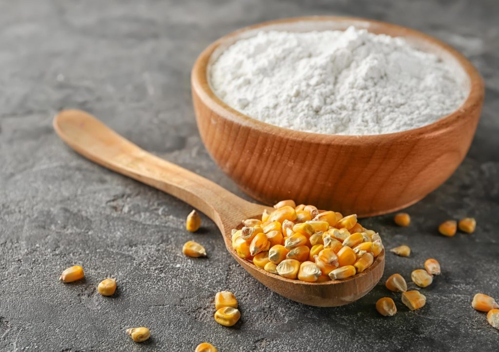 Wooden spoon of corn kernels beside bowl of maltodextrin