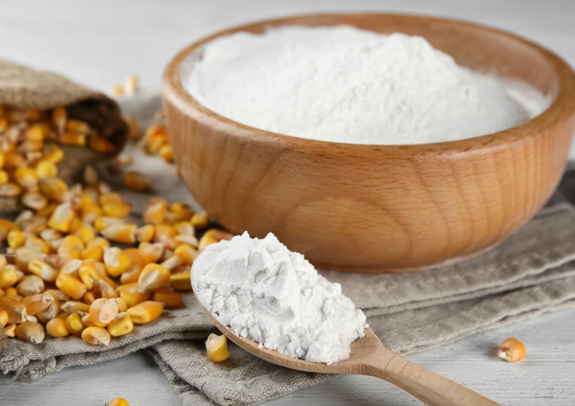Scoop of maltodextrin with corn kernels and wooden bowl