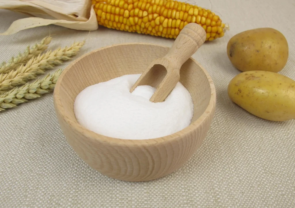 Wooden bowl of dextrose powder beside corn