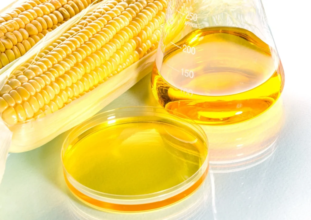 Corn kernels beside glassware filled with golden high fructose corn syrup