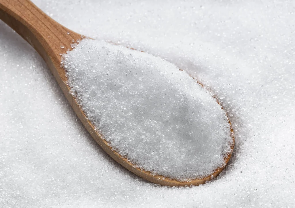 Coarse granulated erythritol on a wooden spoon, commonly used as a sugar substitute in baking and beverages.
