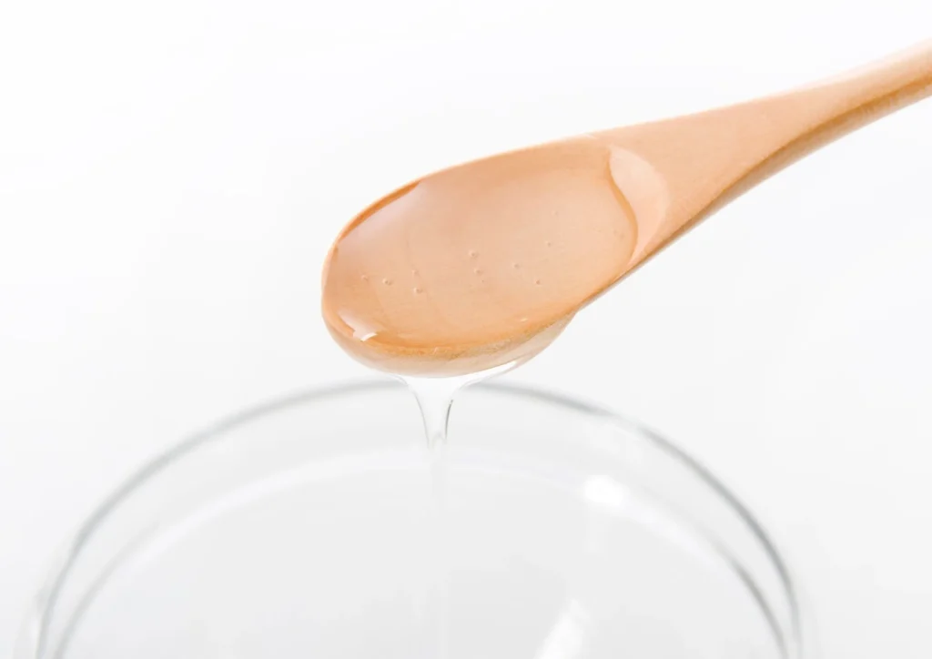 Liquid sucrose dripping from a wooden spoon into a glass bowl.