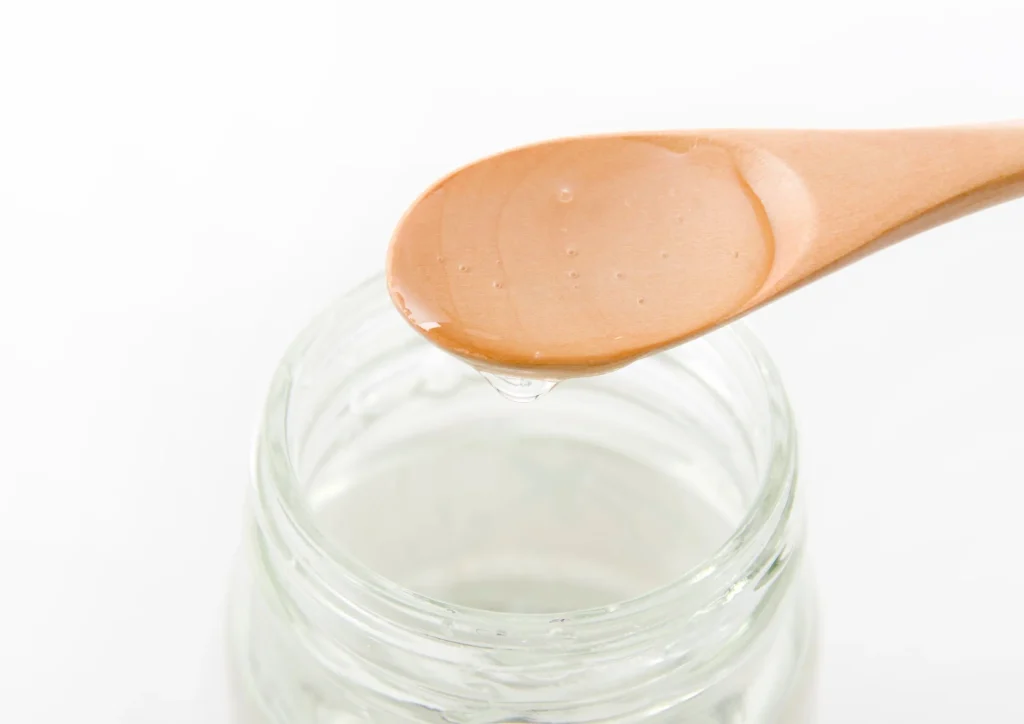 Wooden spoon with liquid sucrose dripping over a glass jar.
