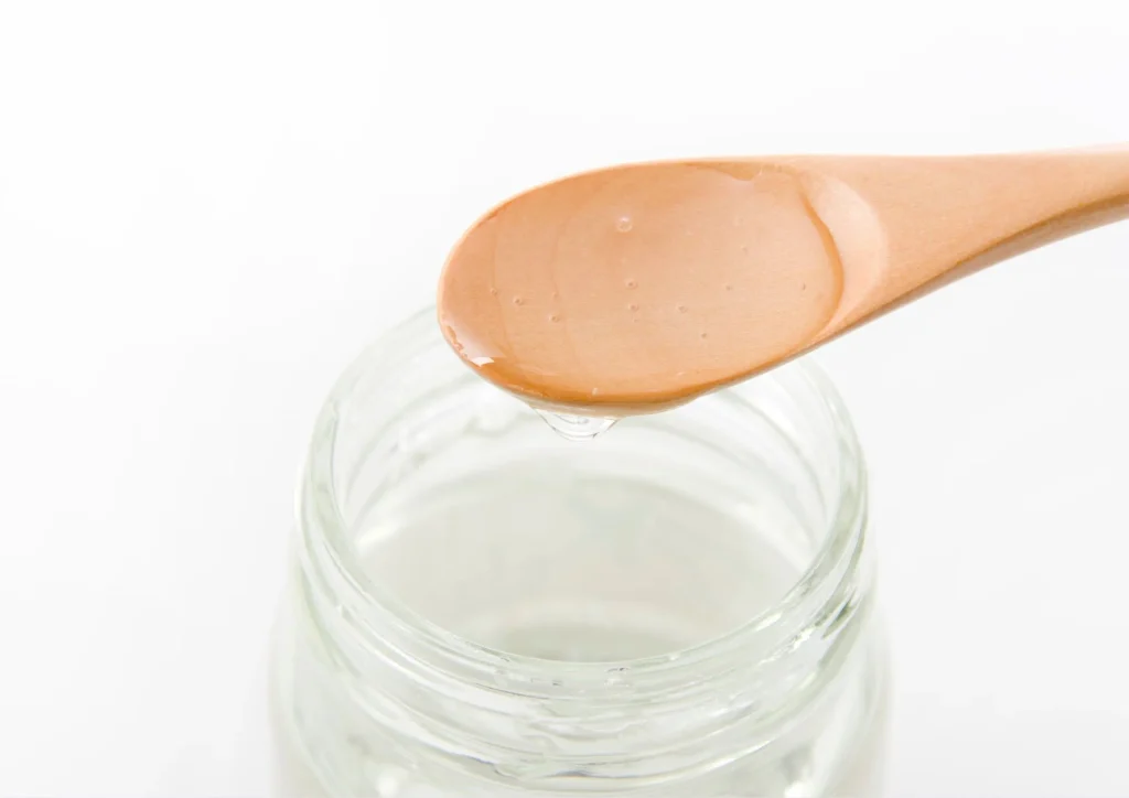 Clear maltitol syrup dripping from a wooden spoon over a glass jar, commonly used in sugar-free confections.