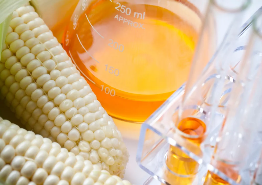 Non-GMO high fructose corn syrup in lab glassware beside corn.